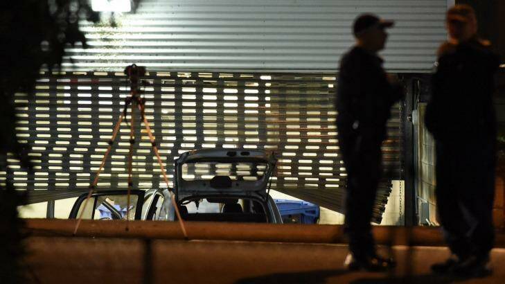 Officers examine the scene where a fire-damaged car rammed into a police roller door. Photo: Wolter Peeters
